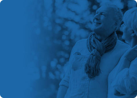 Image of a senior couple walking outdoors. They are smiling up at something outside the frame of the image.